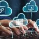 Illustration of cloud computing services with interconnected cloud icons, servers, software, and computer systems displayed above a person typing on a laptop keyboard.