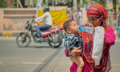 Woman holding a child and offering water during hot weather on a city street, illustrating the human impacts of extreme heat and humidity in India.