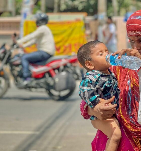 Woman holding a child and offering water during hot weather on a city street, illustrating the human impacts of extreme heat and humidity in India.