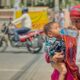 Woman holding a child and offering water during hot weather on a city street, illustrating the human impacts of extreme heat and humidity in India.