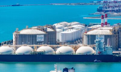 LNG import terminal with large liquefied natural gas storage tanks and an LNG carrier docked at a coastal port.