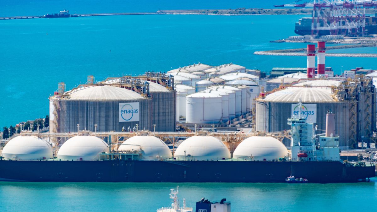 LNG import terminal with large liquefied natural gas storage tanks and an LNG carrier docked at a coastal port.