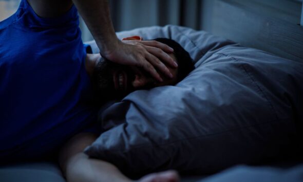 A person lying awake in bed on a warm night, illustrating sleep loss linked to rising nighttime temperatures.