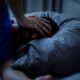 A person lying awake in bed on a warm night, illustrating sleep loss linked to rising nighttime temperatures.