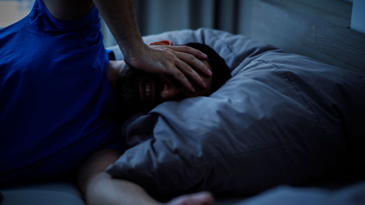 A person lying awake in bed on a warm night, illustrating sleep loss linked to rising nighttime temperatures.