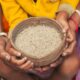 Child and adult hands holding a bowl of rice, symbolising India's food security efforts and the challenge of accessing nutritious diets.