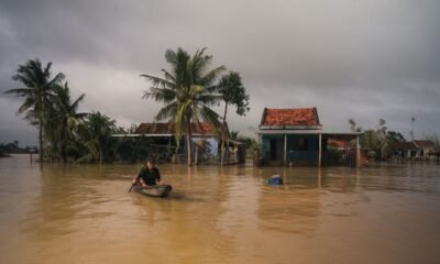 Floodwaters surround homes as a person travels by boat through a submerged village amidst Assam's flood.