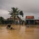 Floodwaters surround homes as a person travels by boat through a submerged village amidst Assam's flood.