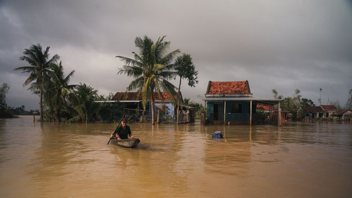 Floodwaters surround homes as a person travels by boat through a submerged village amidst Assam's flood.