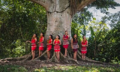 Indigenous women standing beside a large tree in a tropical forest, illustrating the relationship between Indigenous communities and nature conservation