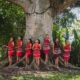Indigenous women standing beside a large tree in a tropical forest, illustrating the relationship between Indigenous communities and nature conservation