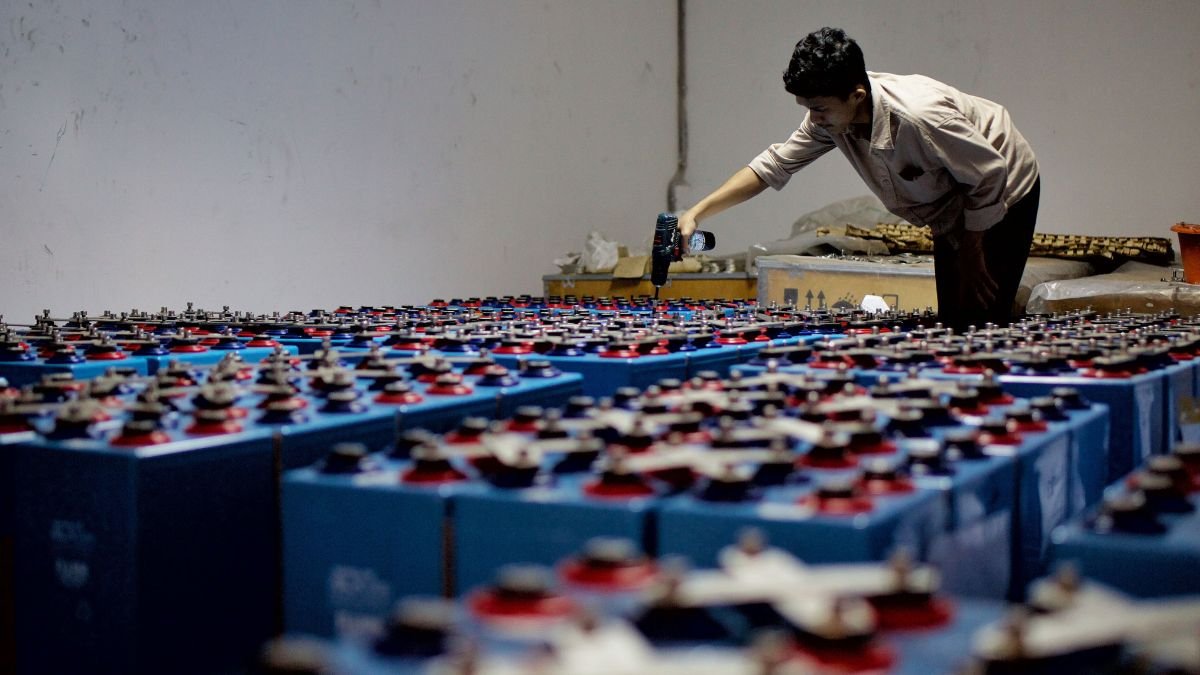 Worker assembling a large array of batteries at an energy storage facility.