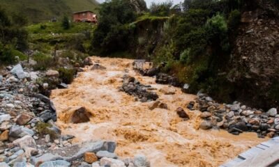 Muddy floodwater rushing through a rocky Himalayan stream near a mountain settlement in Nepal