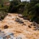 Muddy floodwater rushing through a rocky Himalayan stream near a mountain settlement in Nepal