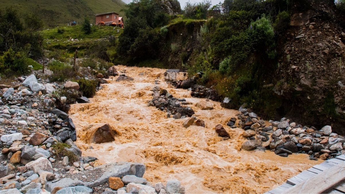 Muddy floodwater rushing through a rocky Himalayan stream near a mountain settlement in Nepal