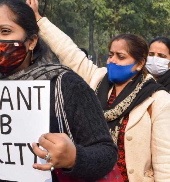 Women wearing masks march in a protest, holding a sign that reads “WE WANT JOB SECURITY.”