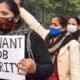 Women wearing masks march in a protest, holding a sign that reads “WE WANT JOB SECURITY.”