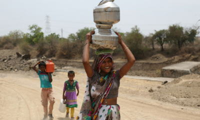 Woman carrying water pots on her head along a dry rural road in India