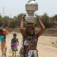 Woman carrying water pots on her head along a dry rural road in India