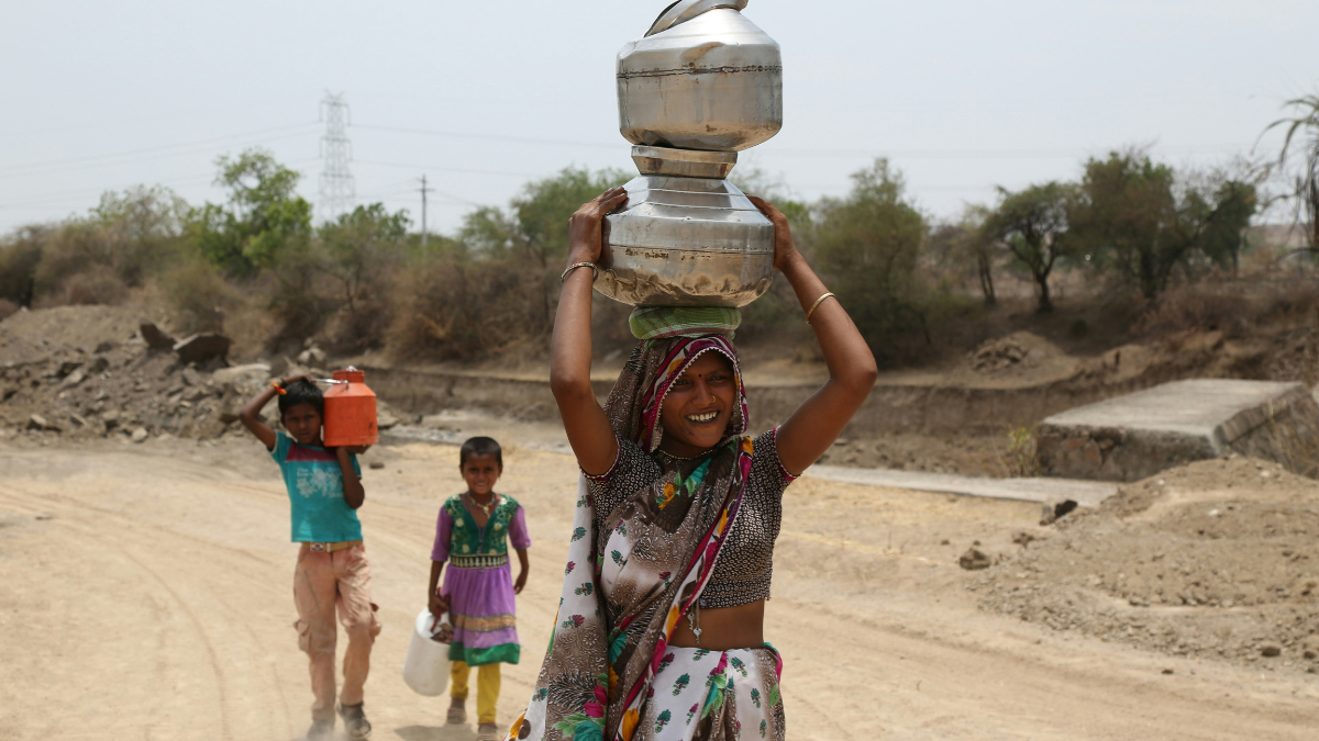 Woman carrying water pots on her head along a dry rural road in India