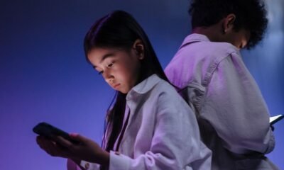 Two teenagers using smartphones in a dimly lit room, highlighting concerns around social media use and child online safety.