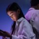 Two teenagers using smartphones in a dimly lit room, highlighting concerns around social media use and child online safety.
