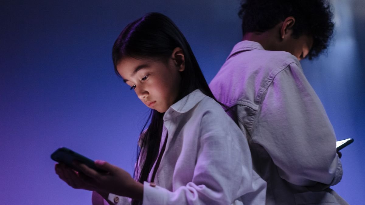 Two teenagers using smartphones in a dimly lit room, highlighting concerns around social media use and child online safety.