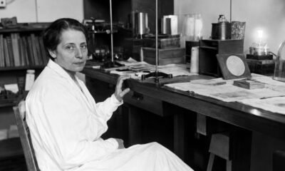 Lise Meitner seated at a laboratory workbench surrounded by scientific equipment
