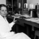 Lise Meitner seated at a laboratory workbench surrounded by scientific equipment