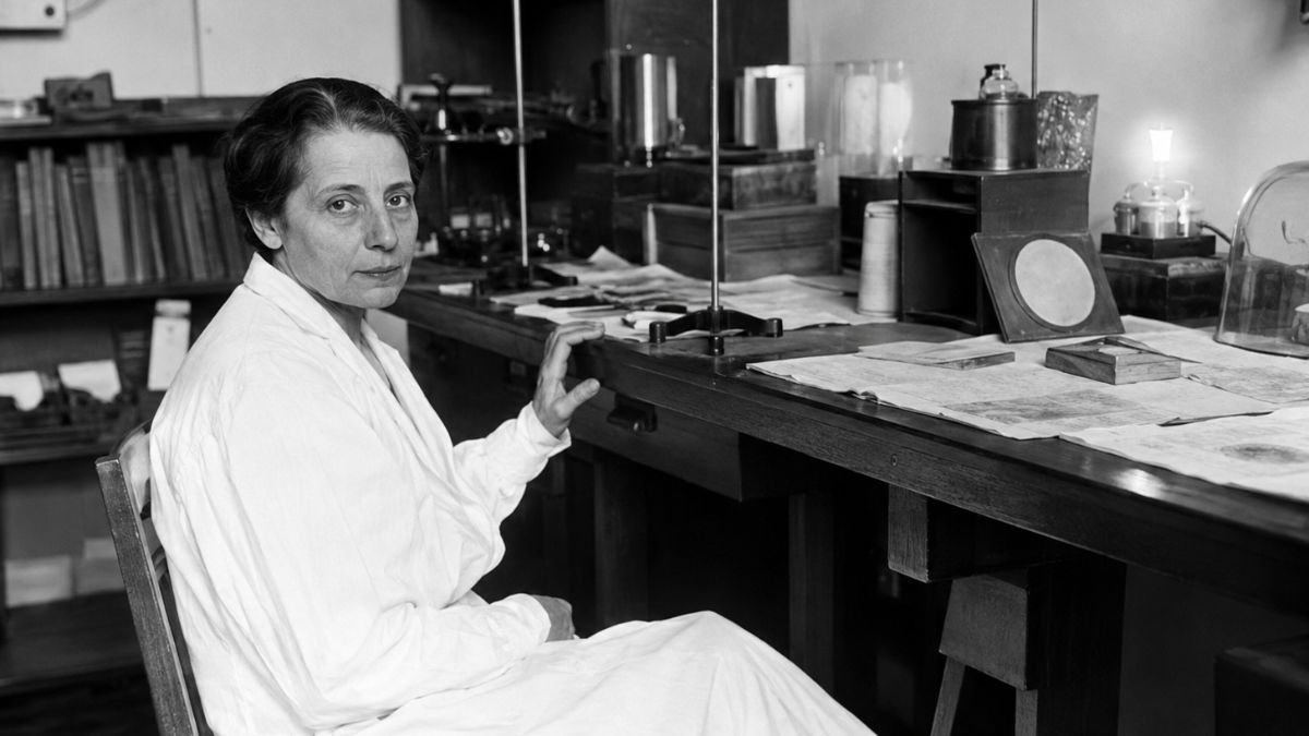 Lise Meitner seated at a laboratory workbench surrounded by scientific equipment