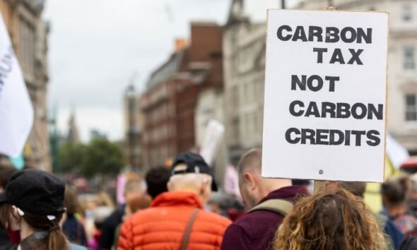 Protester holds a “Carbon Tax Not Carbon Credits” sign as carbon pricing gains importance in global trade