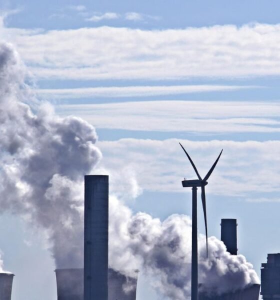 Coal market and coal-fired power plant emitting and smoke beside a wind turbine under a blue sky