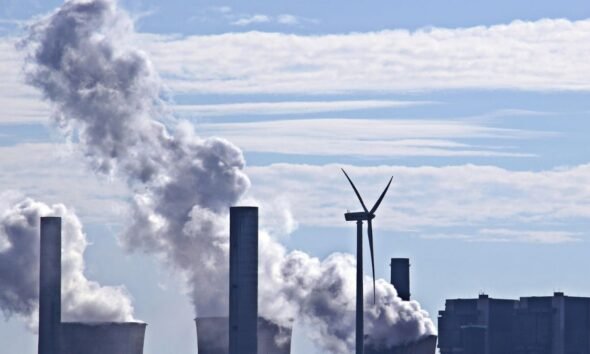 Coal market and coal-fired power plant emitting and smoke beside a wind turbine under a blue sky