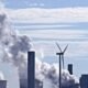 Coal market and coal-fired power plant emitting and smoke beside a wind turbine under a blue sky
