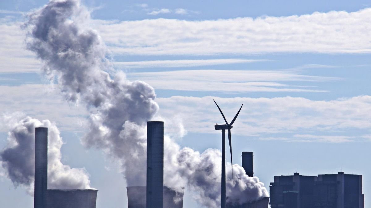 Coal market and coal-fired power plant emitting and smoke beside a wind turbine under a blue sky