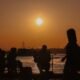 People gather by a waterfront as the sun sets during a period of rising global temperatures
