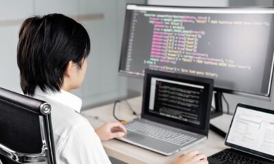 A programmer works at a desk with multiple screens displaying computer code.