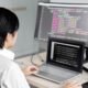 A programmer works at a desk with multiple screens displaying computer code.