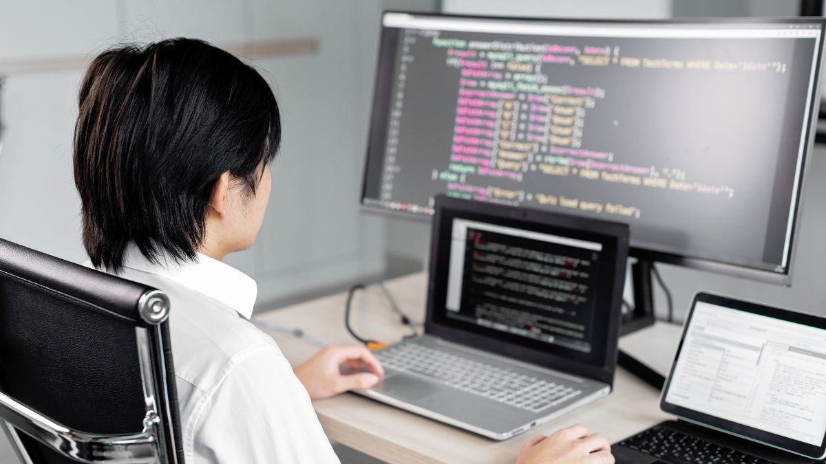 A programmer works at a desk with multiple screens displaying computer code.