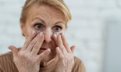 Older woman examining fine lines and wrinkles around her eyes in a mirror