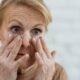 Older woman examining fine lines and wrinkles around her eyes in a mirror