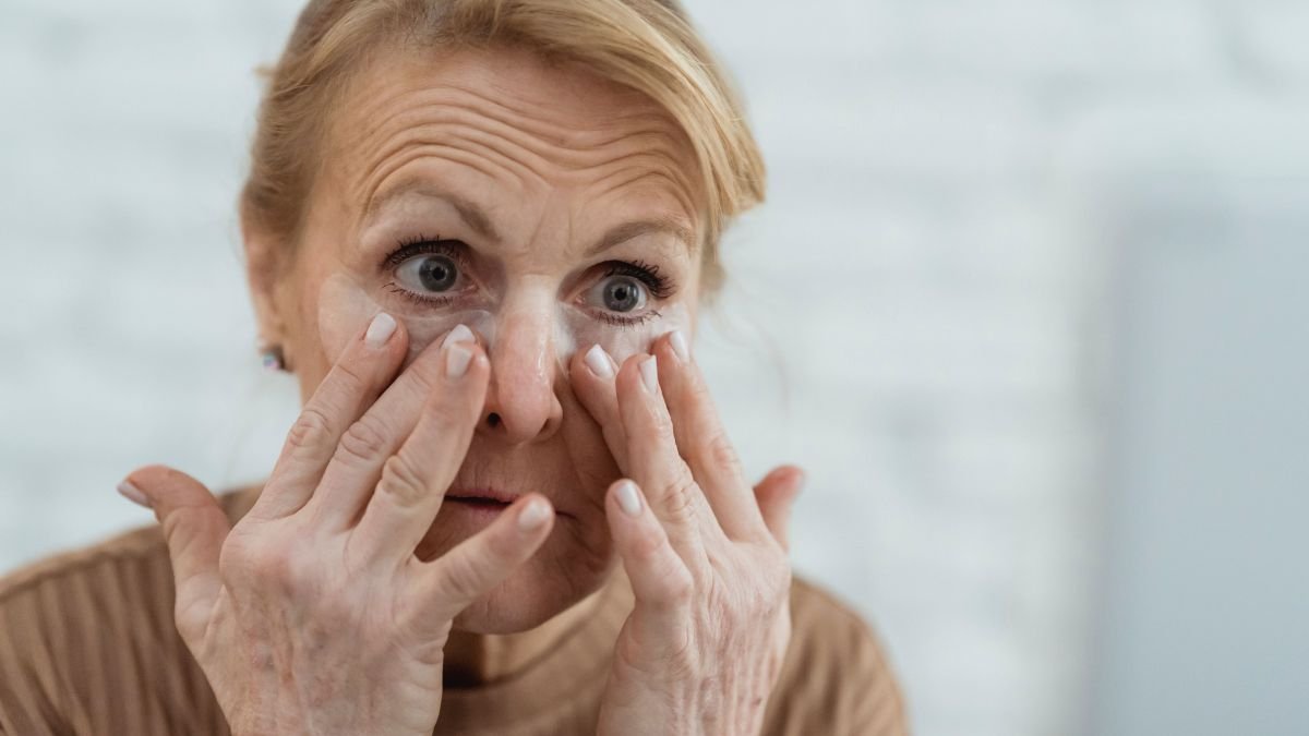 Older woman examining fine lines and wrinkles around her eyes in a mirror