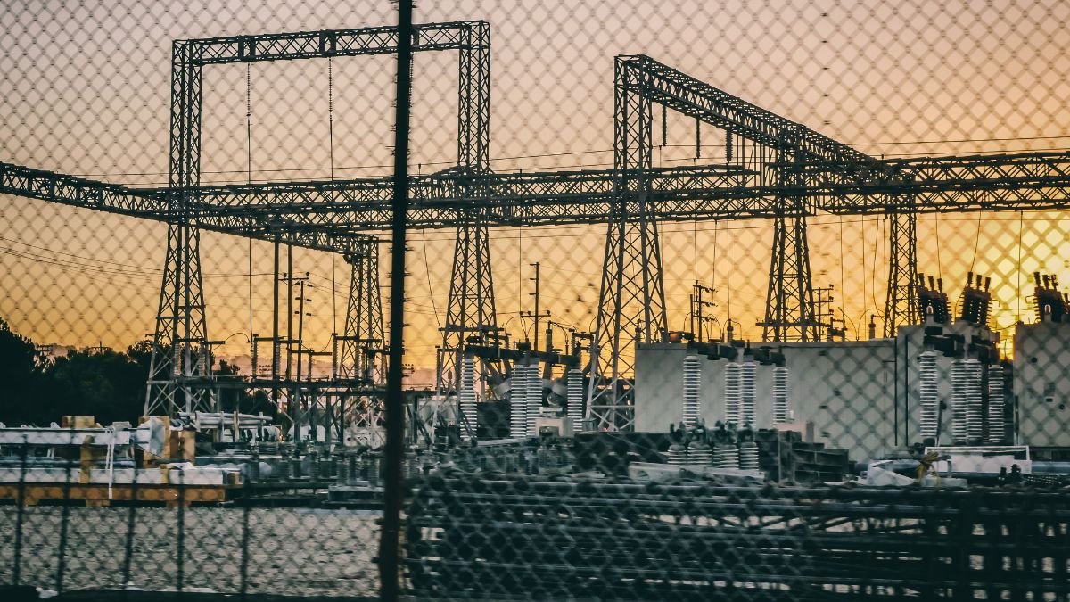 Electrical substation and high-voltage transmission infrastructure against a sunset sky.