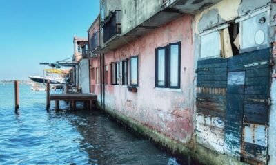 Coastal buildings standing directly beside rising seawater, showing homes and waterfront infrastructure exposed to coastal flooding.