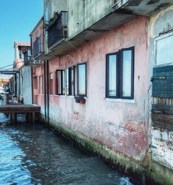 Coastal buildings standing directly beside rising seawater, showing homes and waterfront infrastructure exposed to coastal flooding.