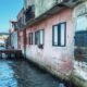 Coastal buildings standing directly beside rising seawater, showing homes and waterfront infrastructure exposed to coastal flooding.