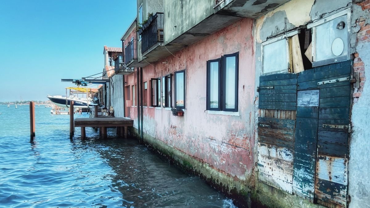 Coastal buildings standing directly beside rising seawater, showing homes and waterfront infrastructure exposed to coastal flooding.