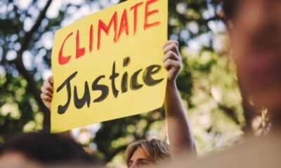 Climate justice protester holding a yellow sign reading “Climate Justice”