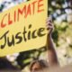 Climate justice protester holding a yellow sign reading “Climate Justice”