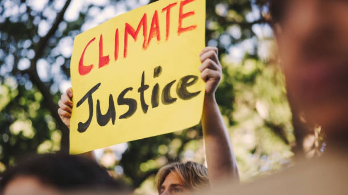 Climate justice protester holding a yellow sign reading “Climate Justice”